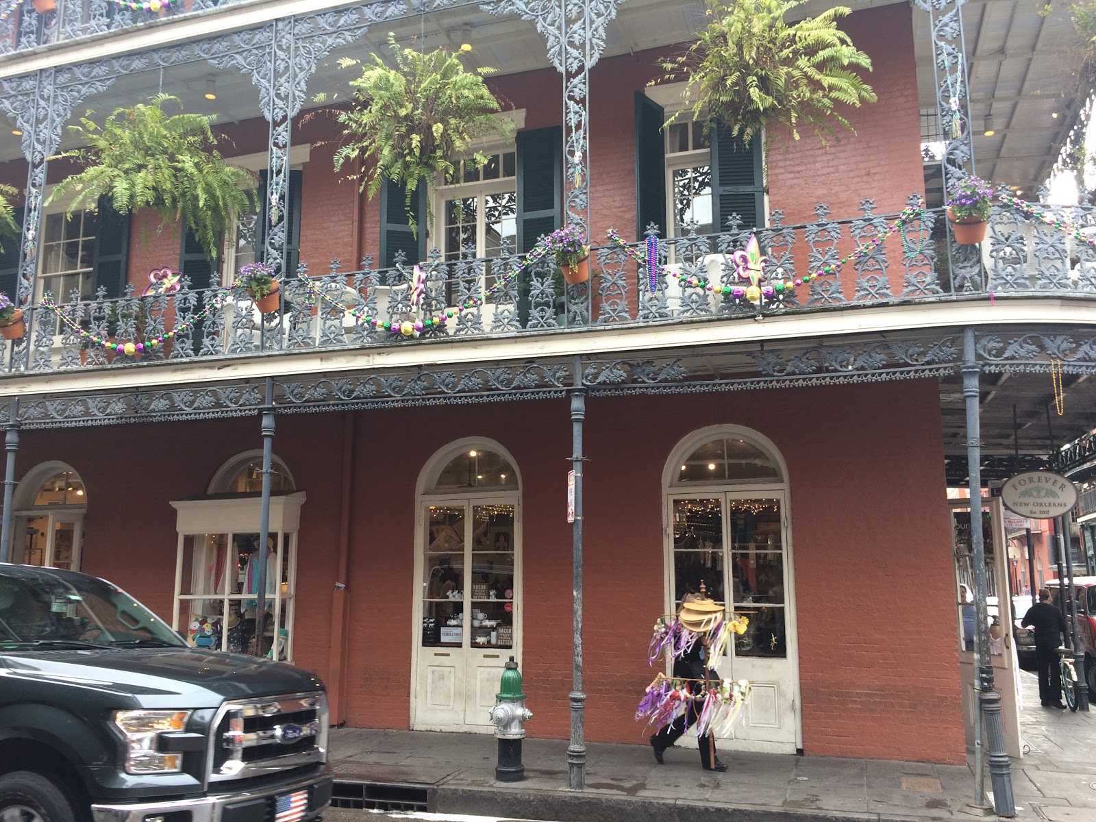 A man walks through the French Quarter streets bearing flowers. Above, Mardi Gras decorations are still hanging up.