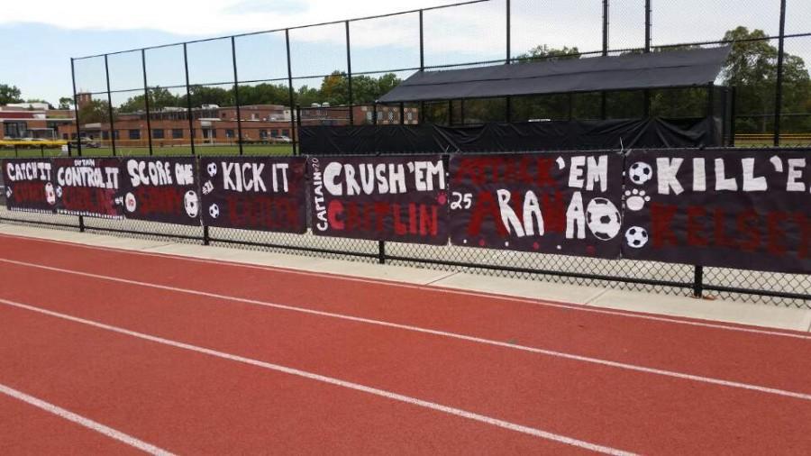 The cheerful signs for senior girls soccer players hang on the football field fence.