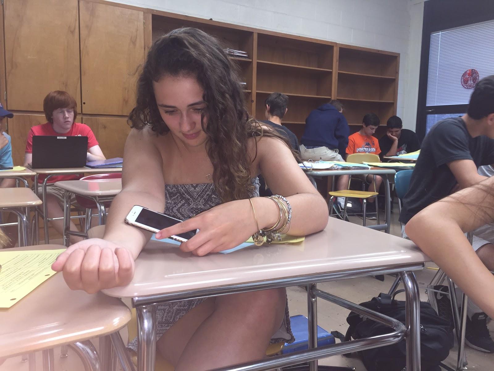 Hallie Johnson (18') puts her iPhone flash to the black ink drawn on her forearm in a classroom.