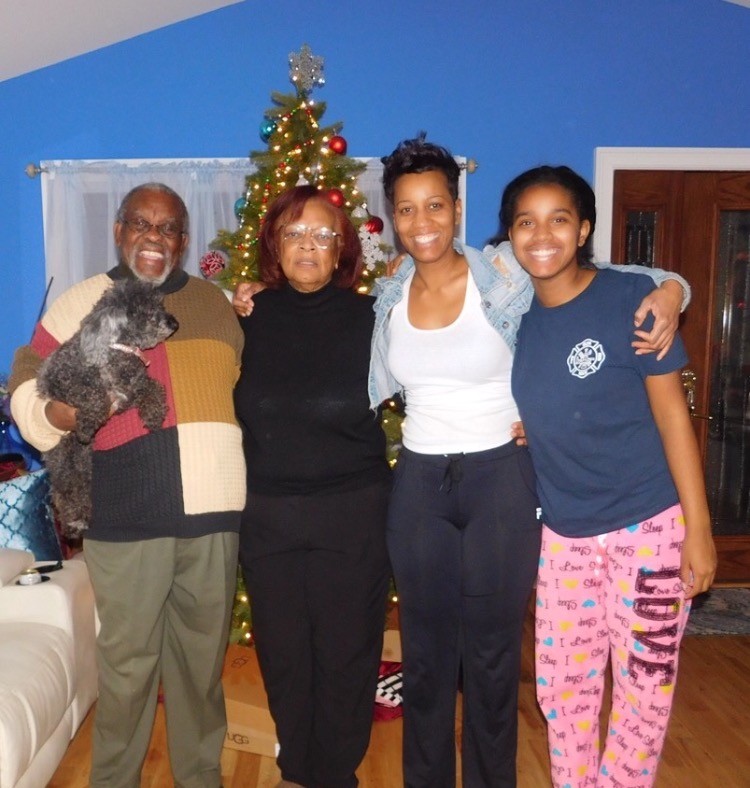 The Greene family stands before their Christmas tree in their newly rebuilt home. Pictured left to right: Irving Greene, their poodle Mocha, Sarah Greene, Charis Greene, and Isis Kirkland.