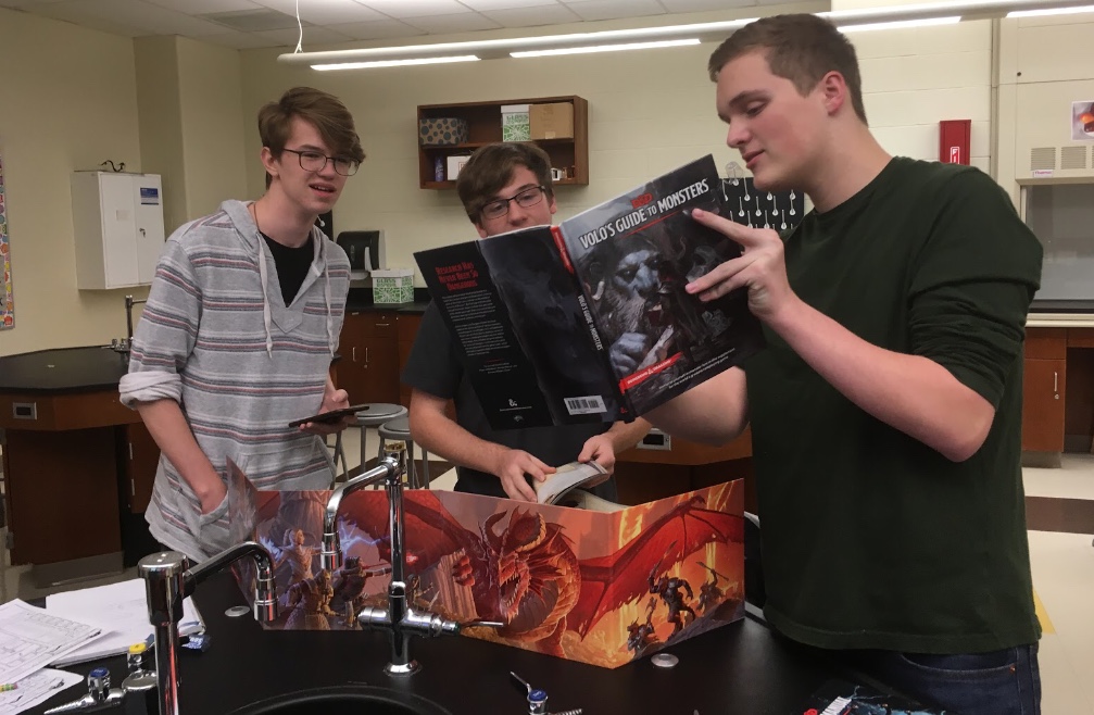 Members Francis Atler, James Ring, and Justus Smith consult Volo's Guide to Monsters before continuing a Dungeons and Dragons campaign.
